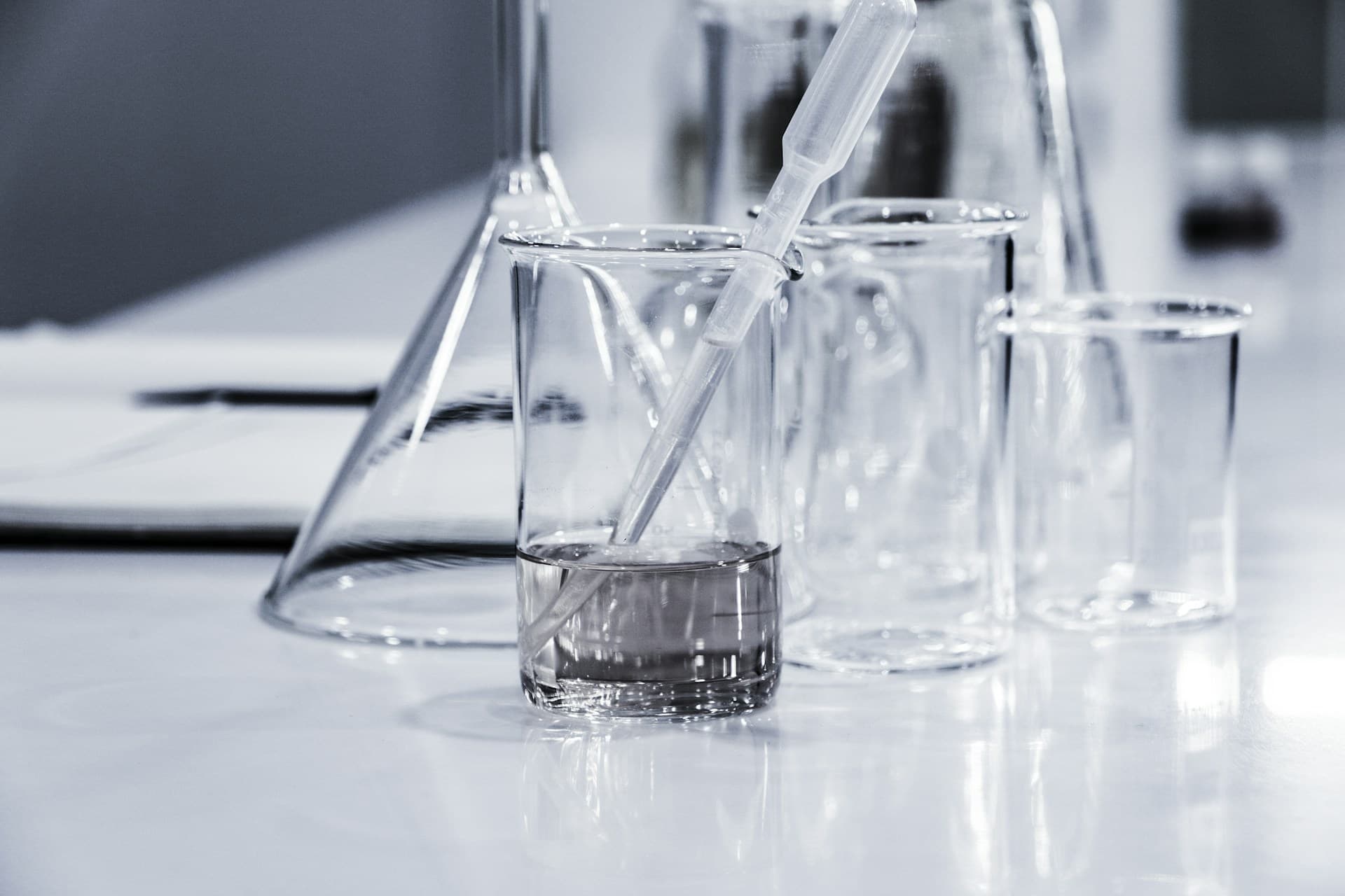 Laboratory beakers and a flask holding clear water-based solutions with a pipette